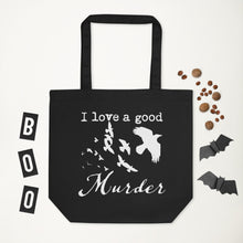 Load image into Gallery viewer, A black tote bag with a white graphic of a murder of crows with the words, "I love a good Murder" laying flat on a white surface with halloween decorations around it.