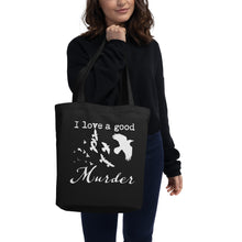 Load image into Gallery viewer, A black tote bag with a white graphic of a murder of crows with the words, "I love a good Murder" is being held up by a woman.