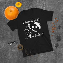 Load image into Gallery viewer, A black graphic tee with a white silhouette of a murder of crows with the words "I love a good Murder" is laying on a gray surface with Halloween decorations around it.
