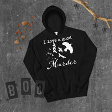 Load image into Gallery viewer, A black hoodie with a white silhouette of a murder of crows in it with the words, "I love a good Murder" is laying on a gray surface with Halloween decorations around it.